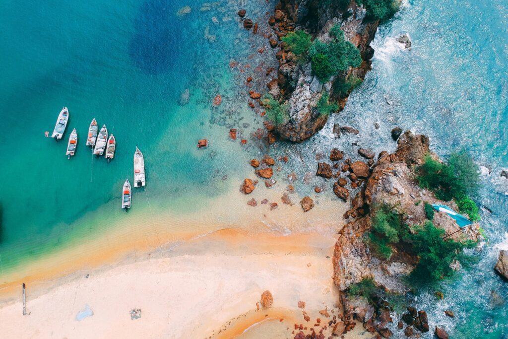 A stunning aerial view of boats anchored by a turquoise beach, showcasing a scenic coastline.