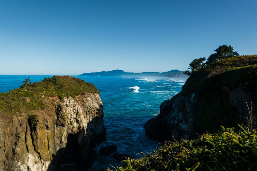Explore a stunning coastal scene featuring dramatic cliffs and a vast blue ocean under a clear sky.