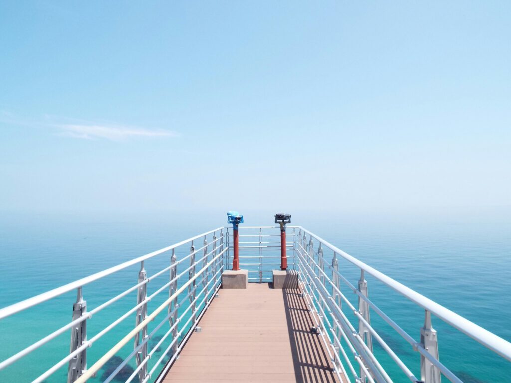 Experience the serenity of a sunny day on a coastal pier overlooking the tranquil sea.