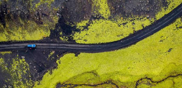 Aerial view of a road cutting through vibrant green moss fields in Southern Iceland, highlighting volcanic terrain.