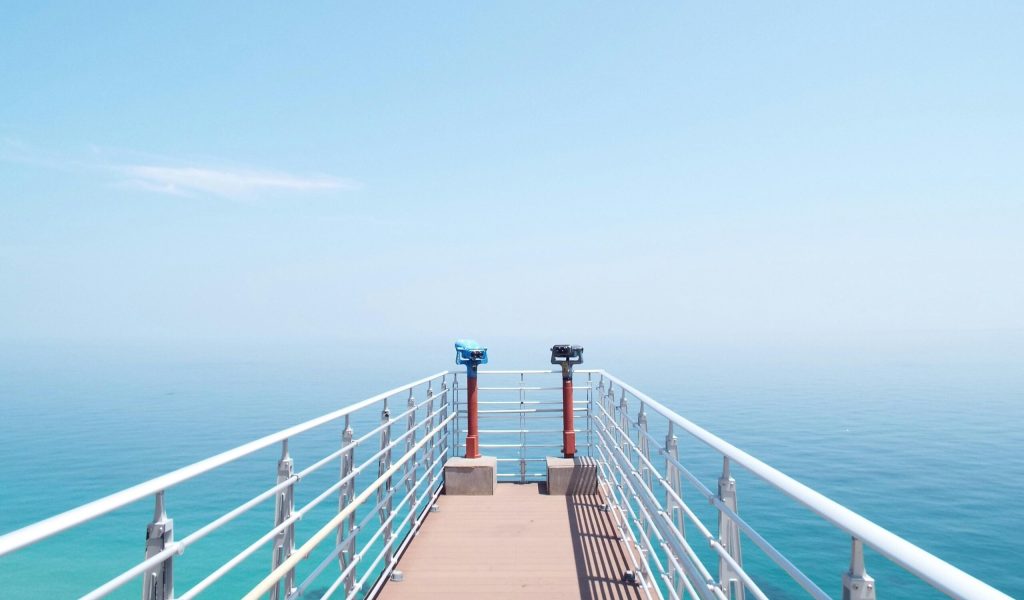 Experience the serenity of a sunny day on a coastal pier overlooking the tranquil sea.