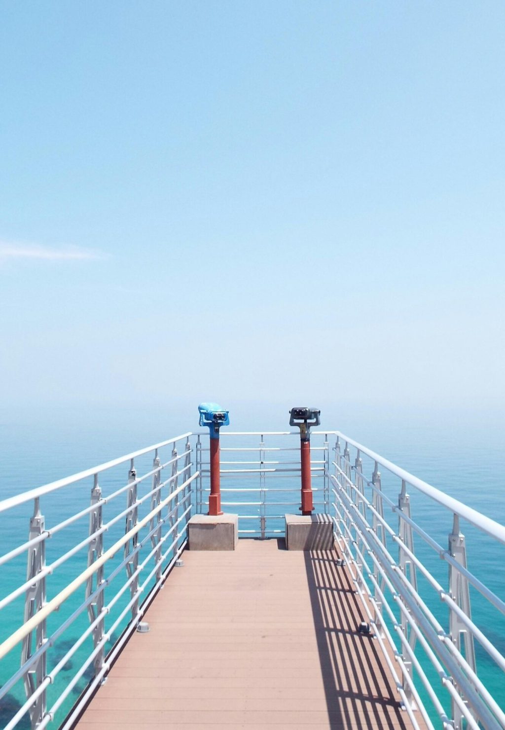 Experience the serenity of a sunny day on a coastal pier overlooking the tranquil sea.