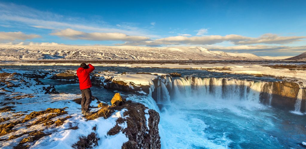 photoghaper taking a photo at godafoss waterfall in winter, icel